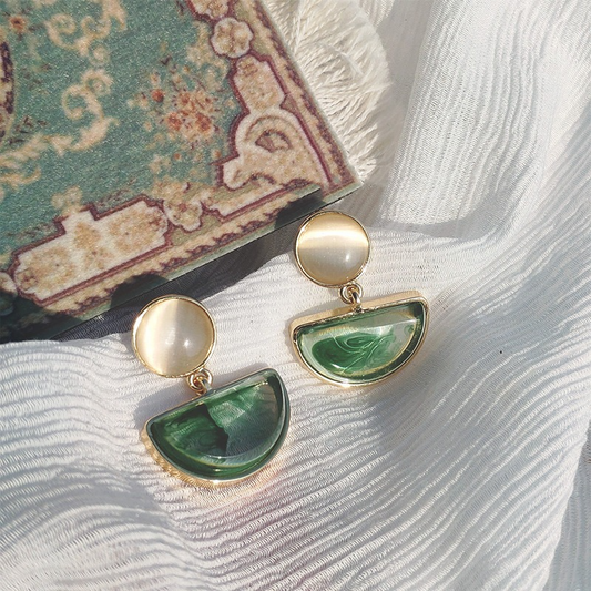 Gold and green earrings on a textured white fabric background