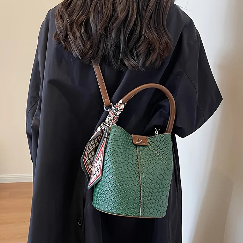 Person wearing a green textured handbag with a patterned strap against a plain background