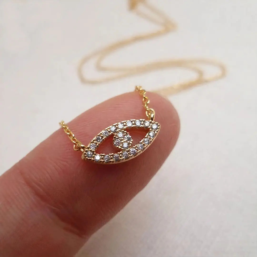 Gold necklace with a leaf-shaped pendant on a finger against a light background
