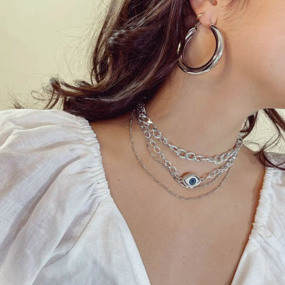 Close-up of a person wearing silver hoop earrings and layered necklaces with an eye pendant.