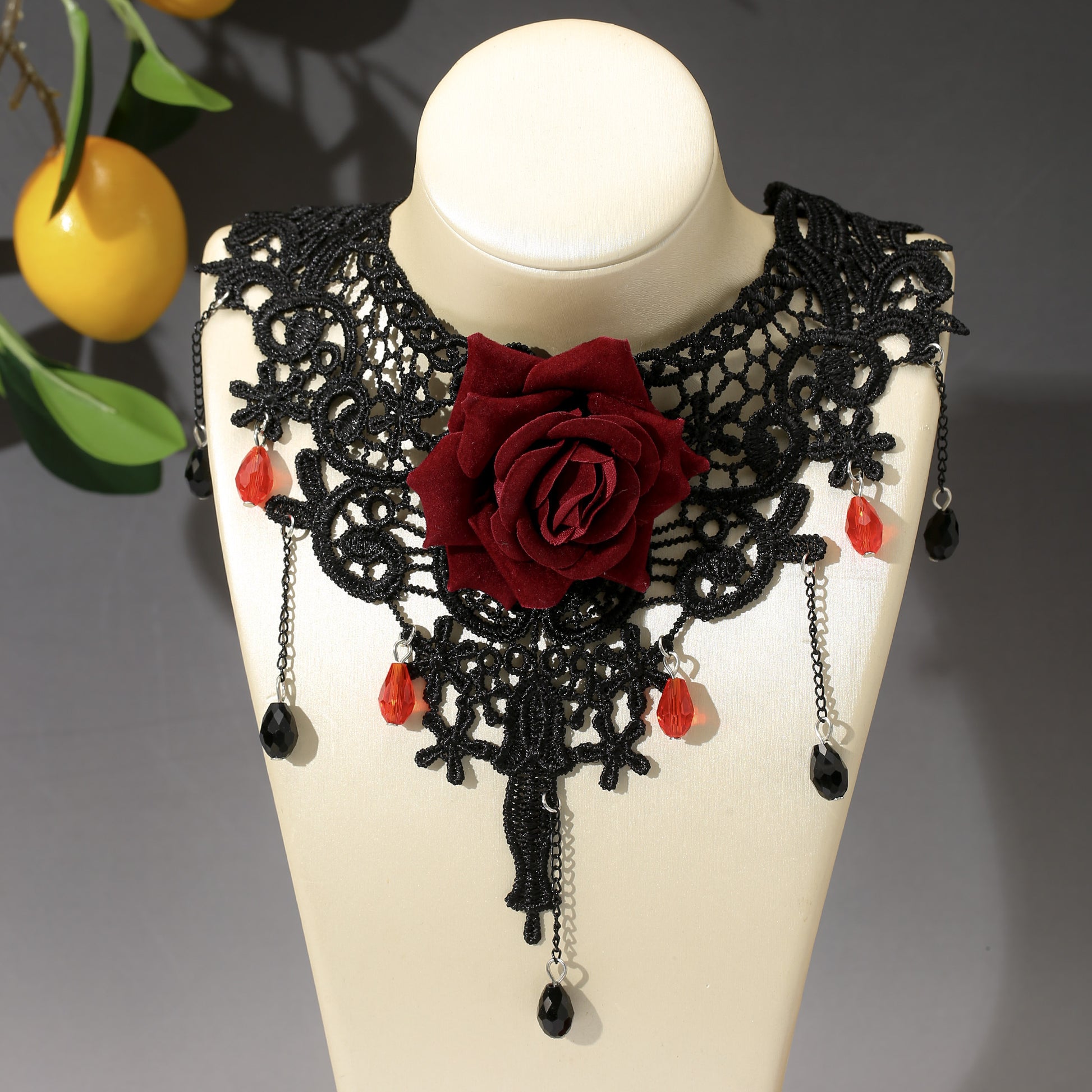 Black lace collar with red rose and beads on a mannequin bust.