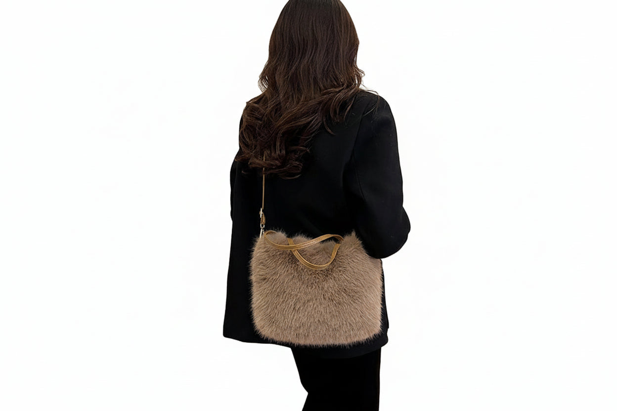 Person wearing a black coat with a fluffy gray bag over their shoulder indoors.