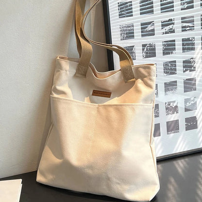 Beige tote bag with a brand label on a surface near a window.