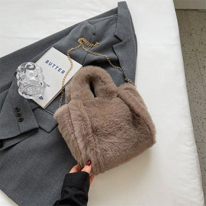 Brown fur handbag held by a hand on a white surface with a gray suit and book in the background.