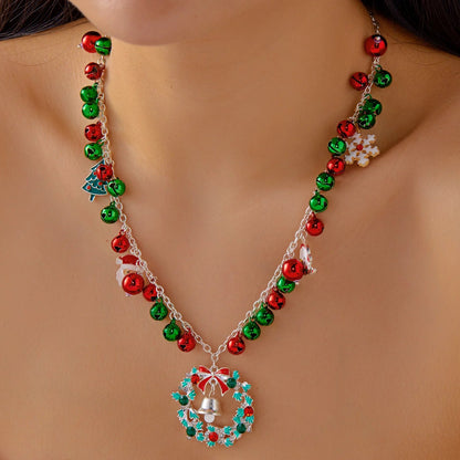 Necklace with red and green beads and a wreath pendant on a person wearing a red garment.