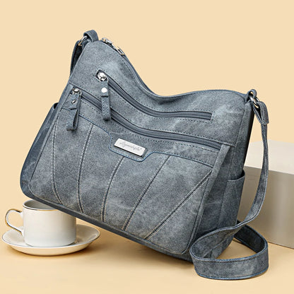 Gray shoulder bag with multiple zippers on a beige background