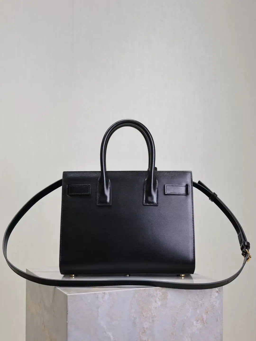Black handbag on a clear stand against a light gray background