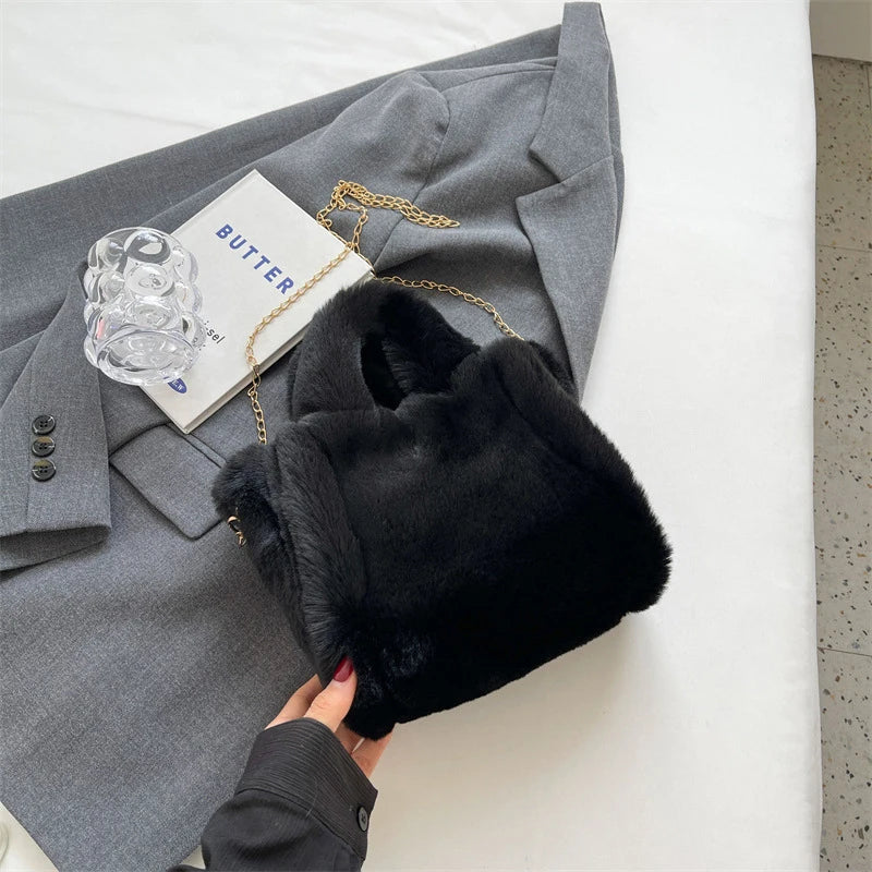 Black fur hat held by a hand next to a gray coat on a white surface