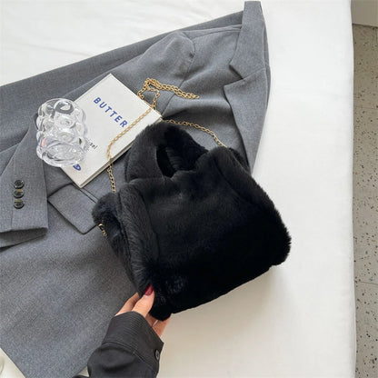 Black fur hat held by a hand next to a gray coat on a white surface