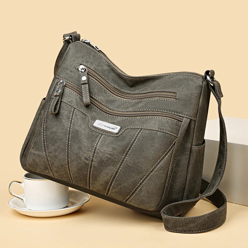 Gray shoulder bag with multiple zippers on a beige background