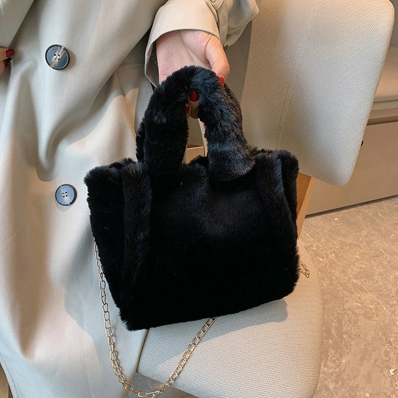 Black fur handbag with chain strap held by a person wearing a beige coat.