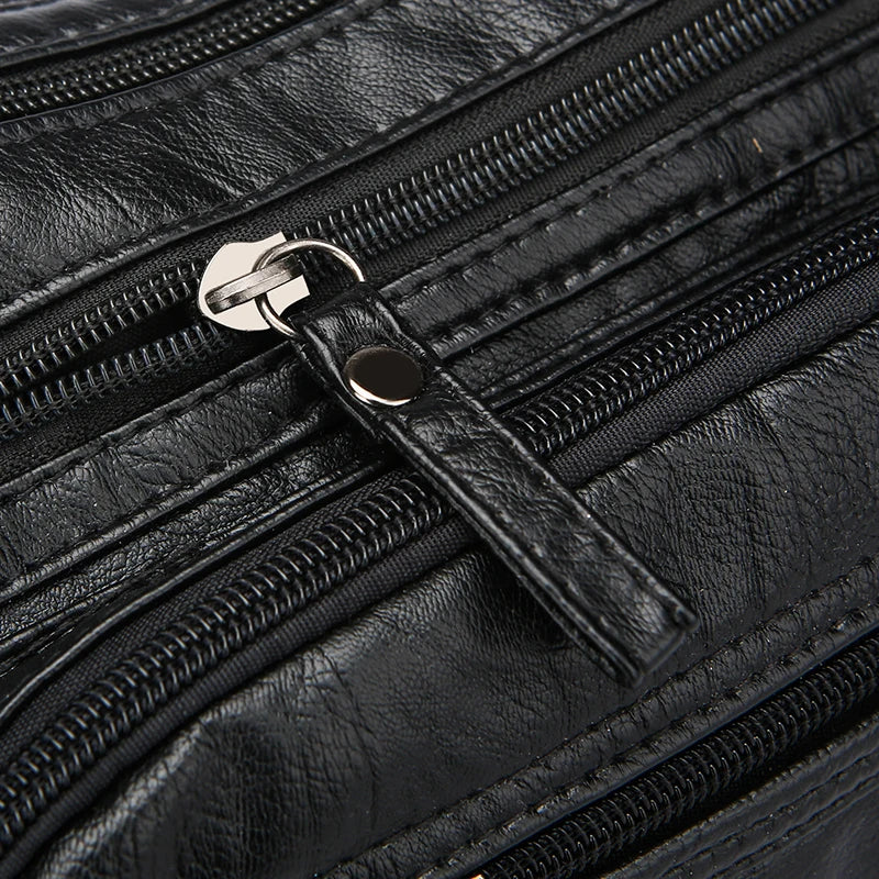 Close-up of a black leather bag with multiple zippers and a handle.