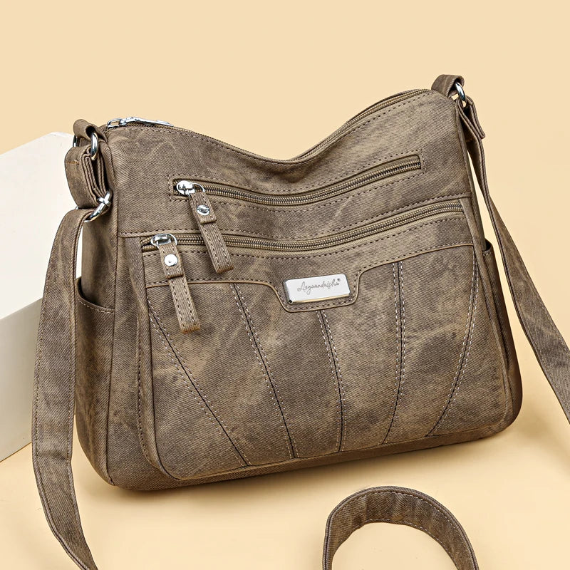 Brown leather handbag with multiple zippers on a beige background