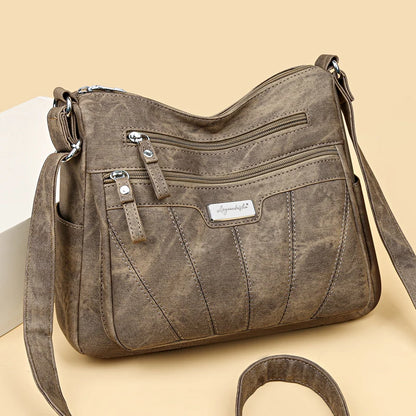 Brown leather handbag with multiple zippers on a beige background