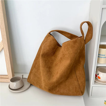 Brown suede handbag on a white surface with a light gray wall and a shelf in the background.