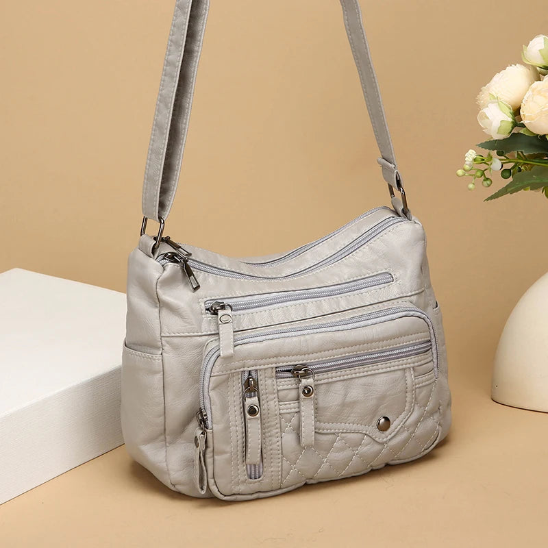 Light gray quilted handbag with multiple zippers on a beige background