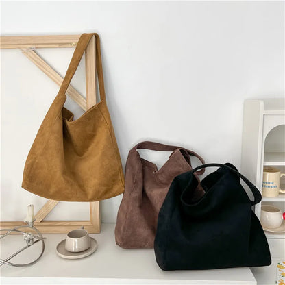 Three suede handbags in brown, beige, and black on a white surface with a light background.