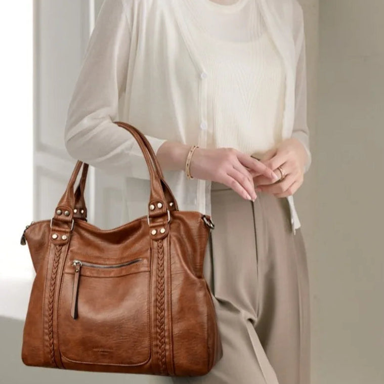Woman holding a brown leather handbag with a plain background