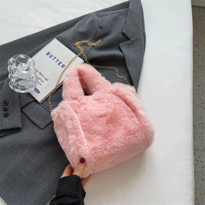 Pink fluffy handbag with gold chain held by a hand on a gray suit jacket and white surface.