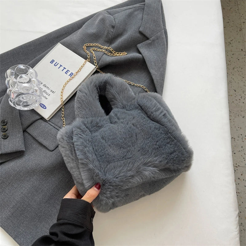 Gray fur handbag held by a hand with a gray coat and book in the background