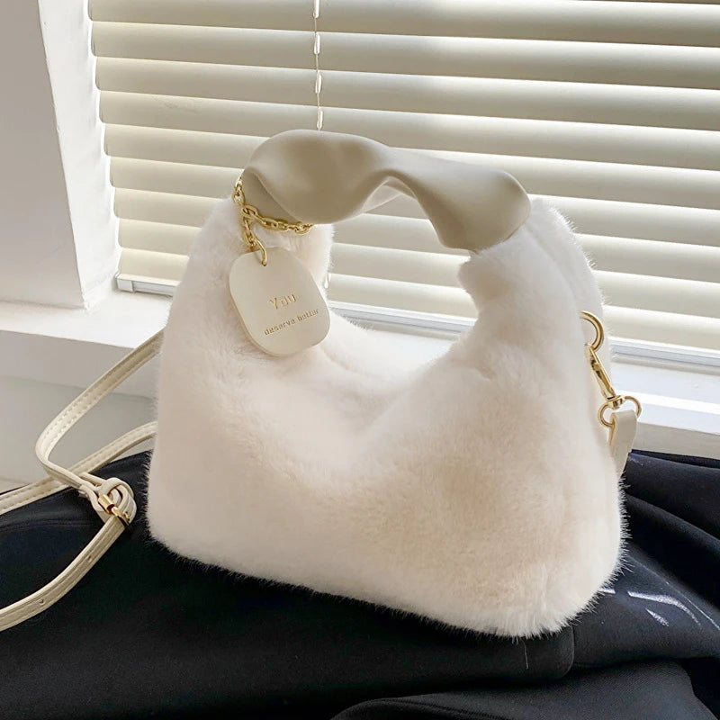 White fluffy handbag with gold accents on a dark surface, blinds in the background