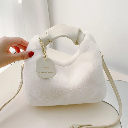 White fluffy handbag with a gold chain and tag held by a hand against a white background