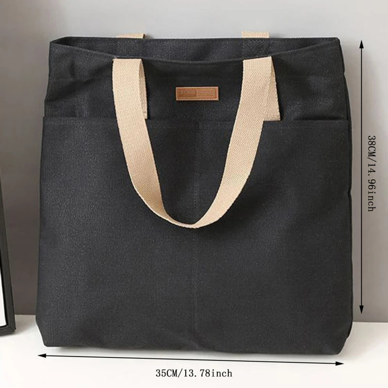 Black tote bag with beige handles and measurements on a gray background