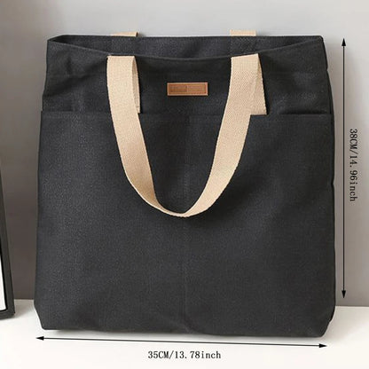 Black tote bag with beige handles and measurements on a gray background