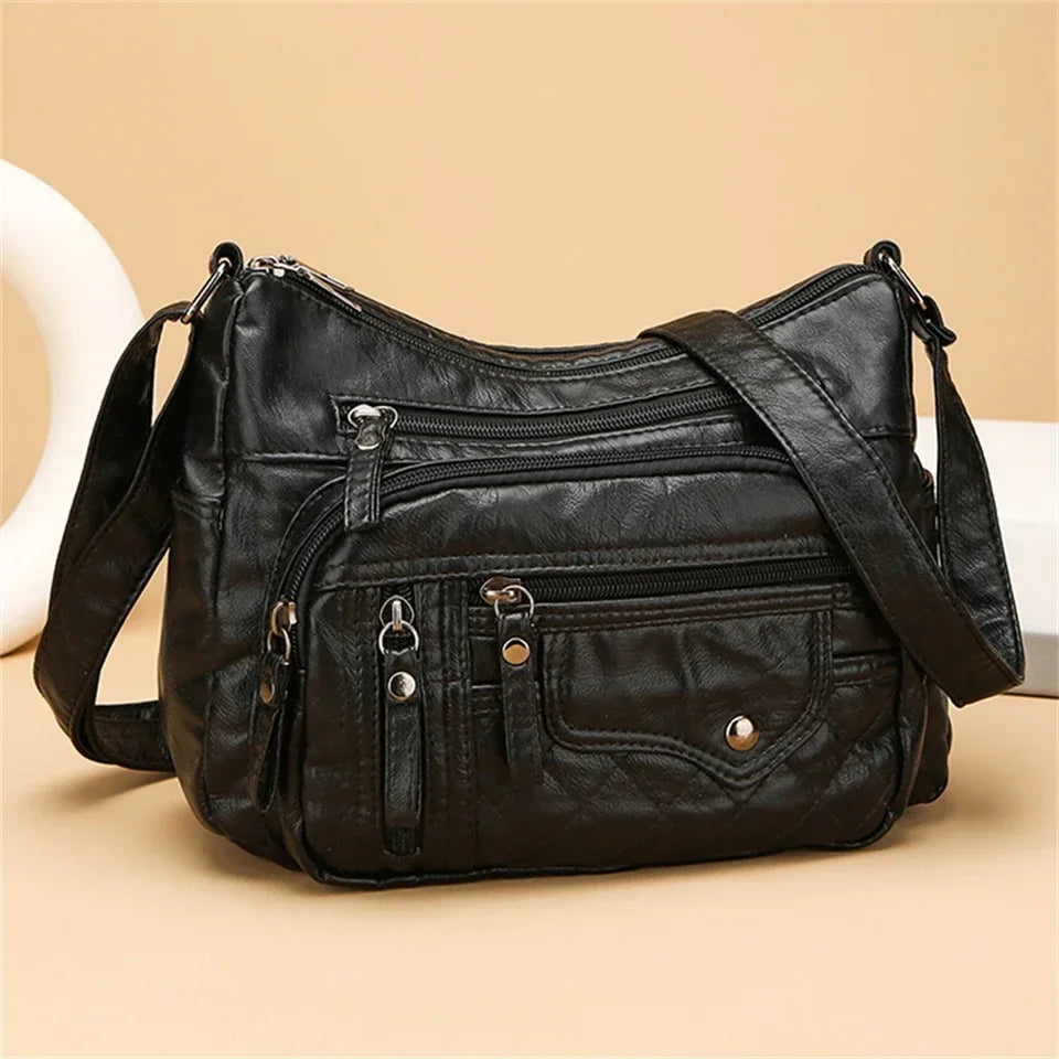 Black leather handbag with multiple pockets and zippers on a beige background