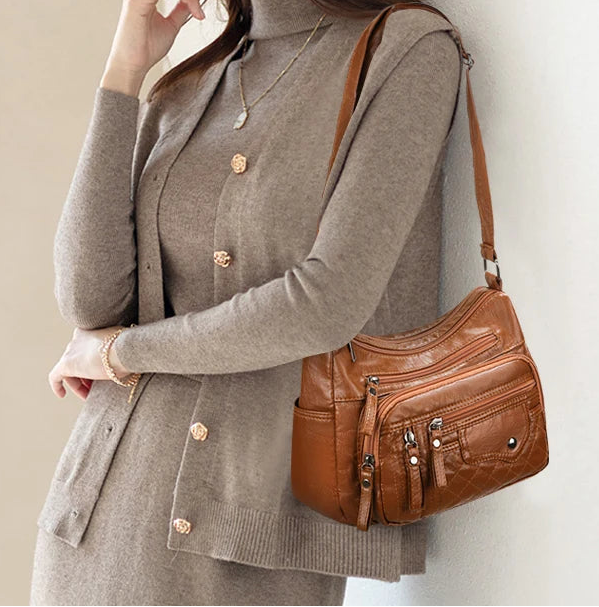 Woman wearing a gray coat with a brown leather handbag against a plain background
