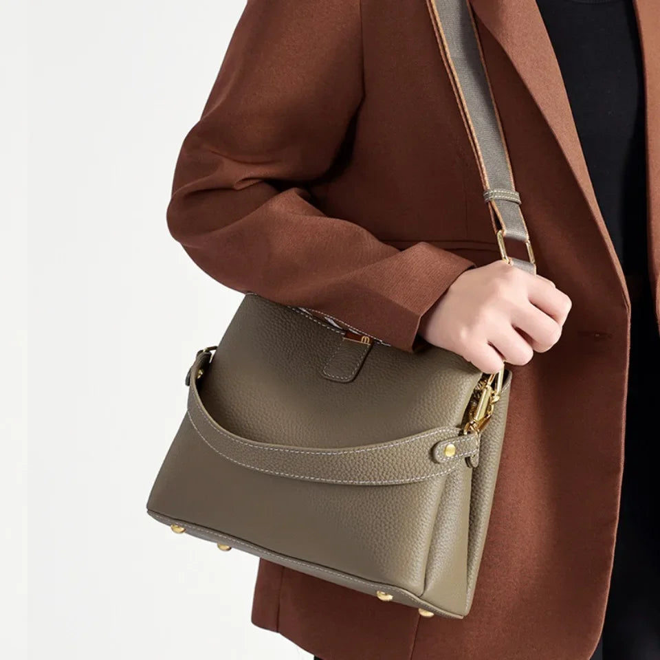 Person holding a brown leather handbag with a plain background