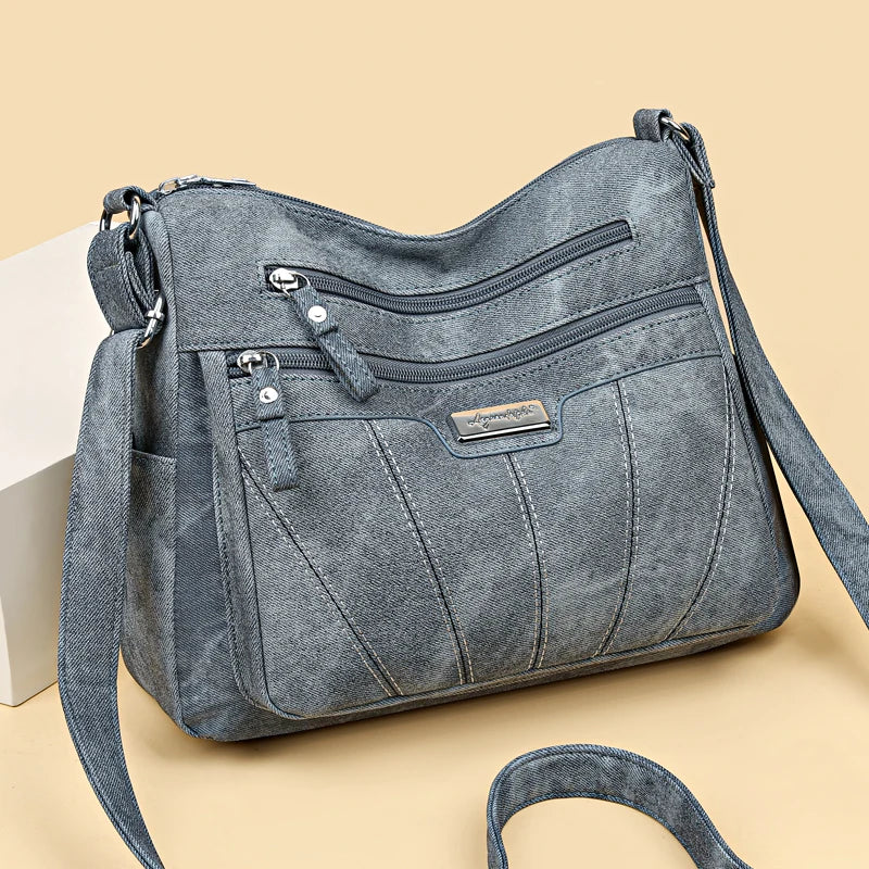 Blue denim handbag with multiple zippers on a beige background