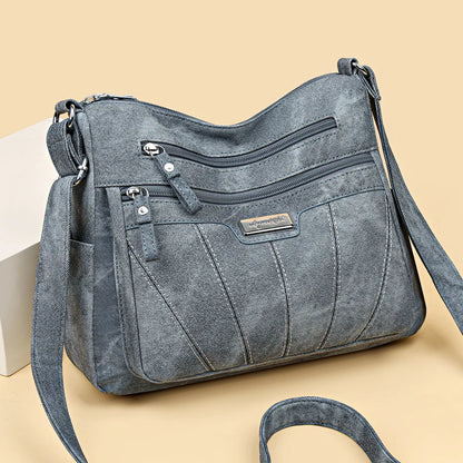 Blue denim handbag with multiple zippers on a beige background