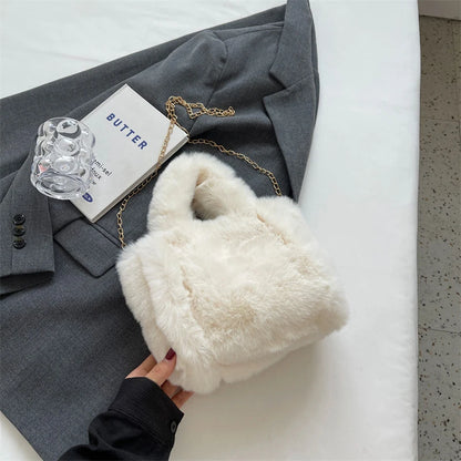 White fluffy handbag held by a hand on a gray suit jacket with a glass and book on a white surface.