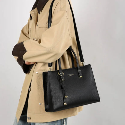 Person holding a black handbag with a beige coat against a light gray background