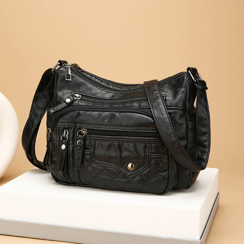 Black leather handbag with multiple pockets and zippers on a beige background