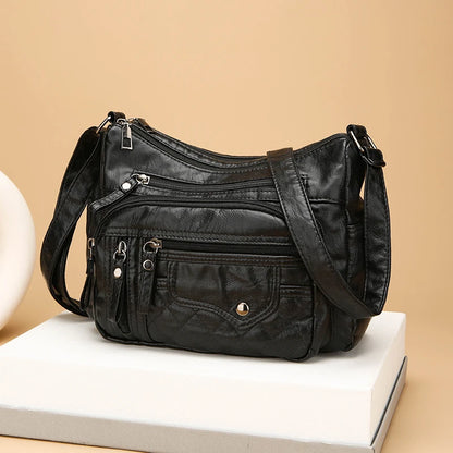 Black leather handbag with multiple pockets and zippers on a beige background