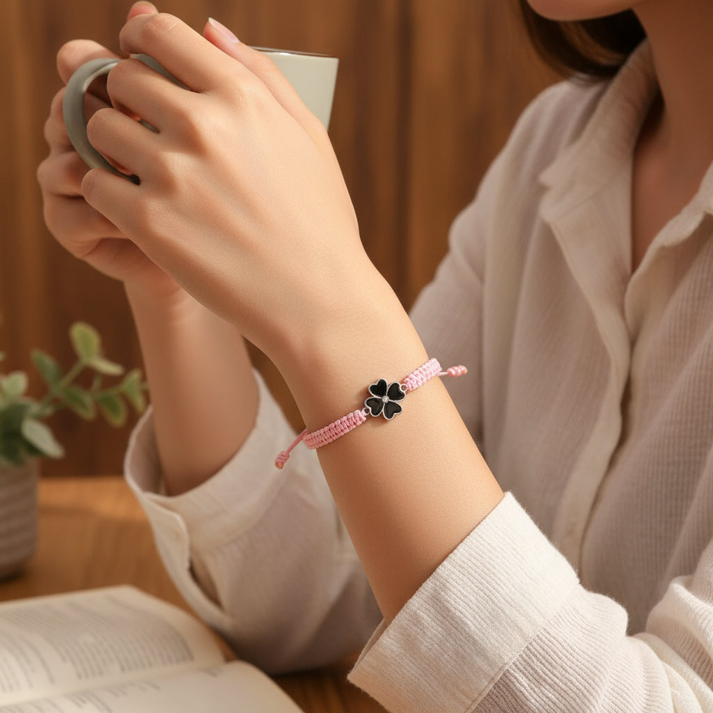 Pink braided bracelet with a black and white clover charm on a white background