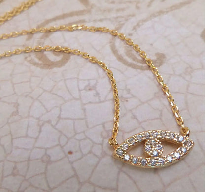 Gold necklace with an eye-shaped pendant on a textured beige background